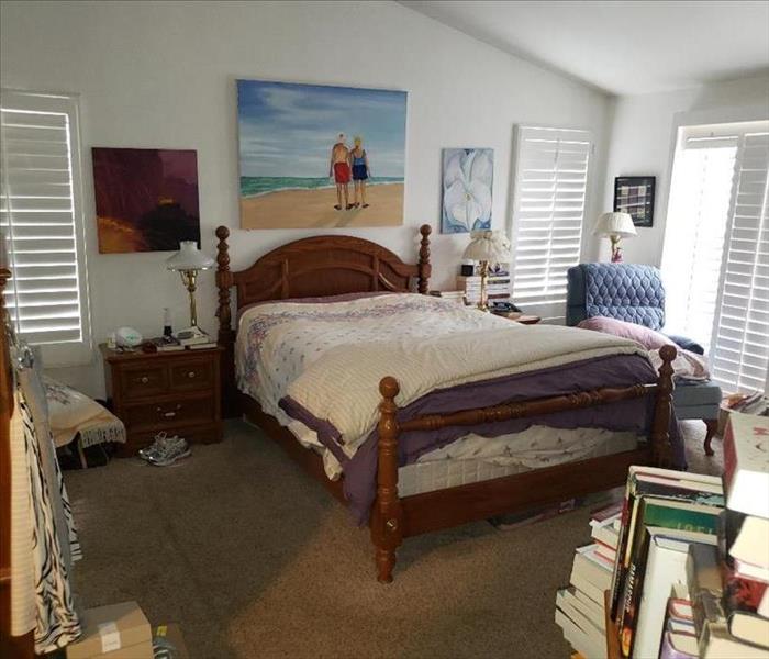 A furnished bedroom with a picture hanging on the wall. Books and knick-knacks around the room